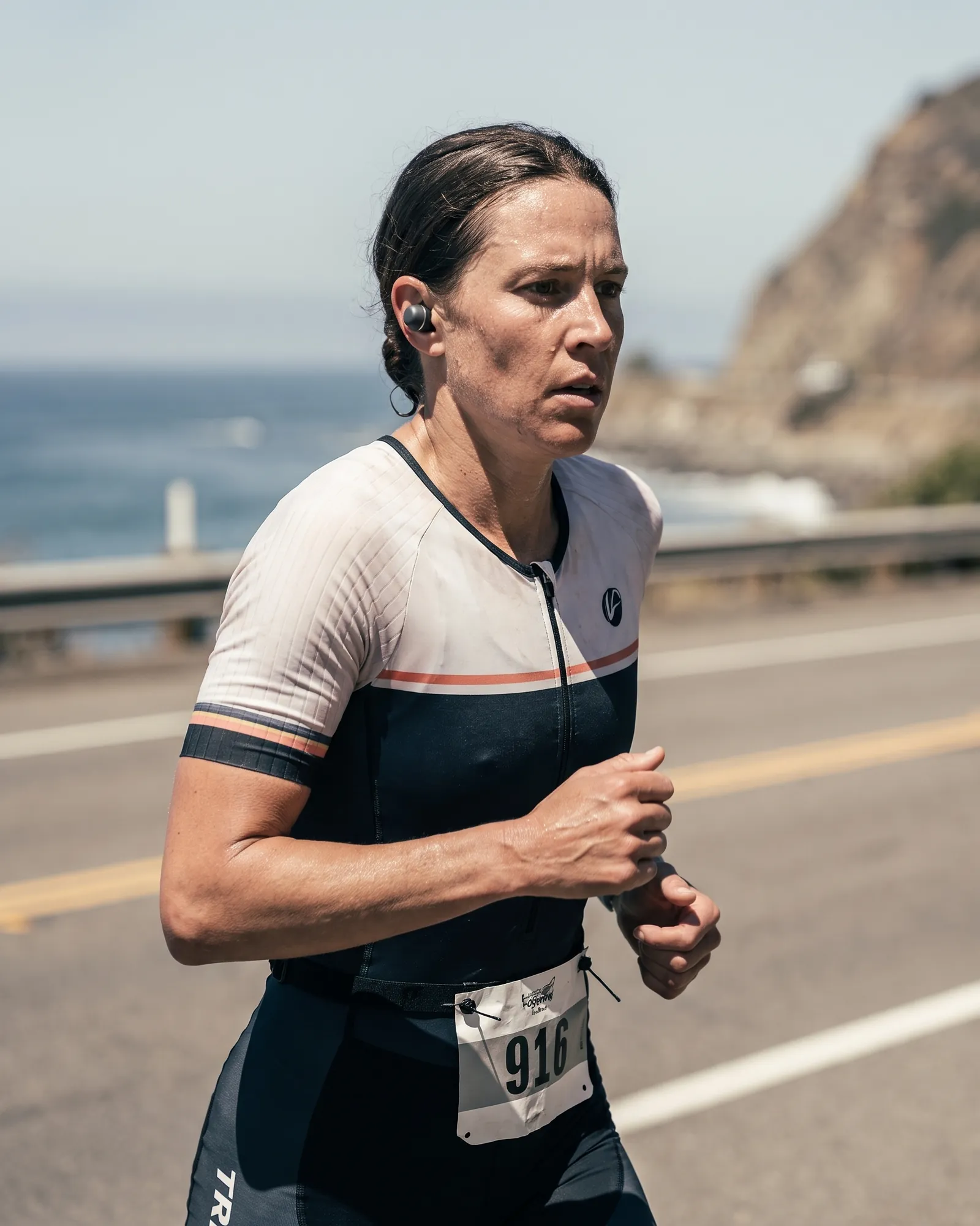 An endurance athlete running on a coastal road during a race in bright midday sun.